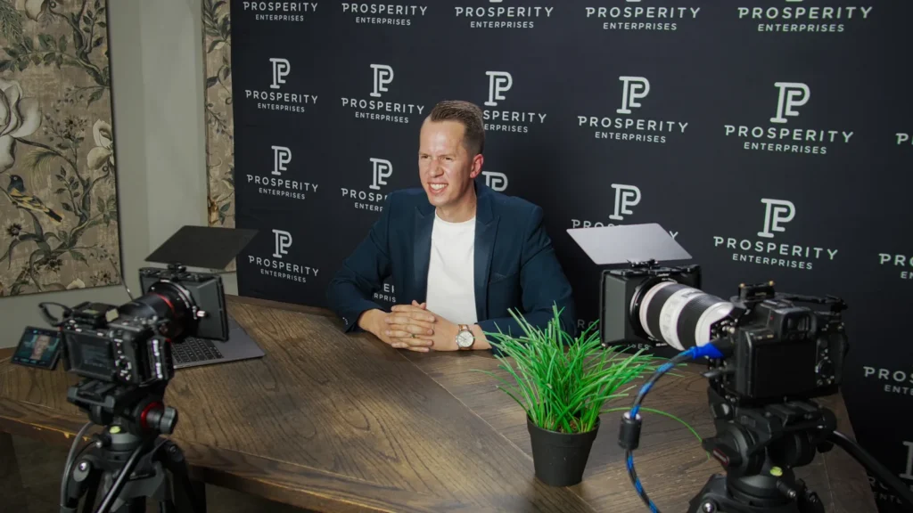 Prosperity Enterprises webinar host between two cameras at the branded backdrop